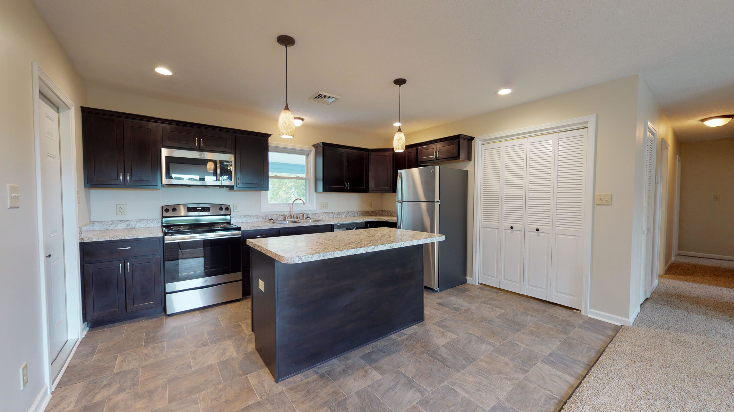 Rehabilitated kitchen featuring dark wood cabinets, granite countertops, a center island, and stainless steel appliances.
