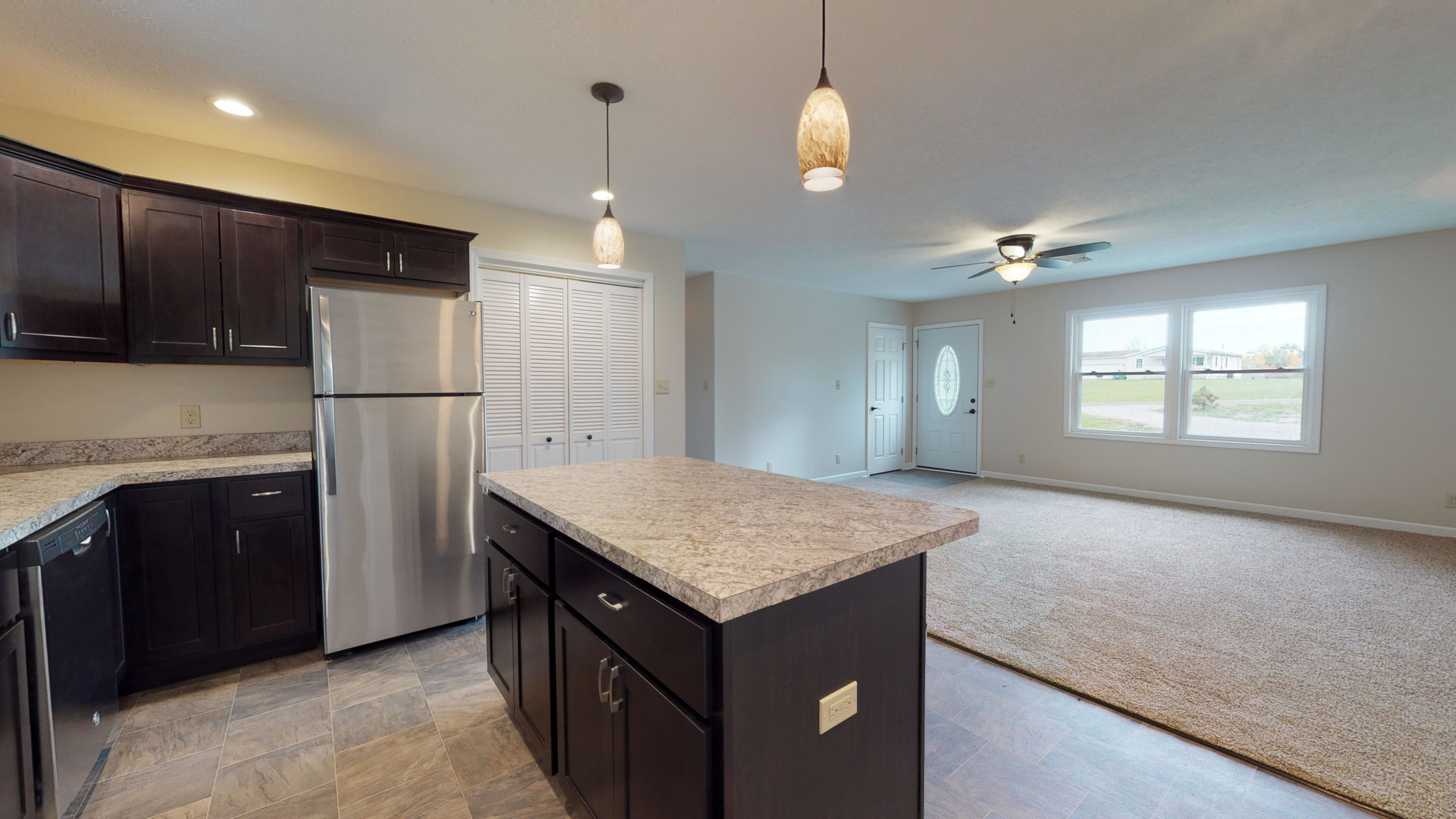 Renovated open floor plan showing the kitchen island looking into a bright, carpeted living room with a ceiling fan.