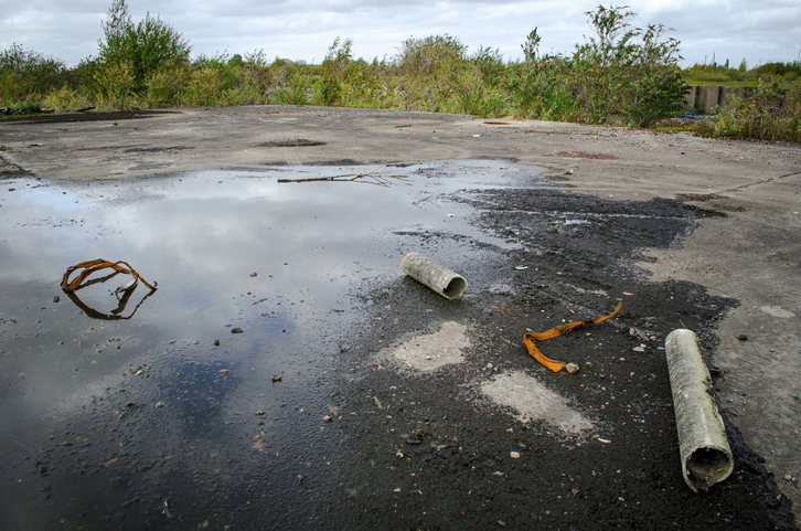 Abandoned industrial site with standing water and debris, showing a vacant lot needing cleanup and redevelopment.