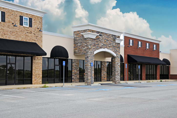 Modern retail storefronts with brick and stone facades, black awnings, and an empty parking lot on a cloudy day.