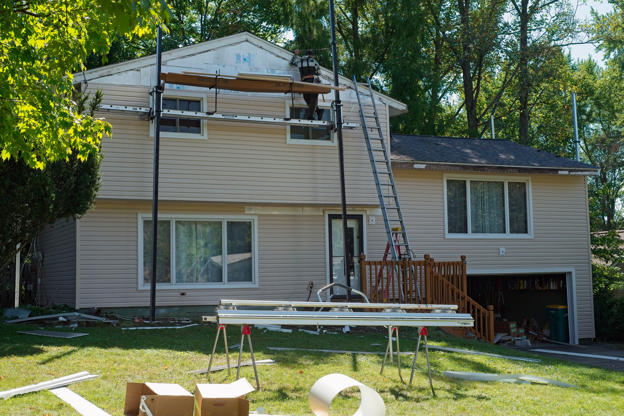 A worker on scaffolding installs new tan siding on a two-story home during a Land Bank renovation project.